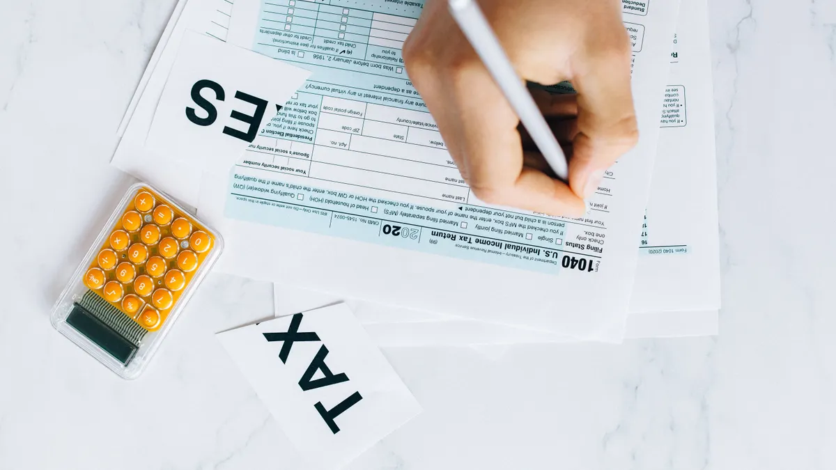 Estimated taxes for self-employed filers: who has to pay them Hand filling out a tax form with calculator nearby