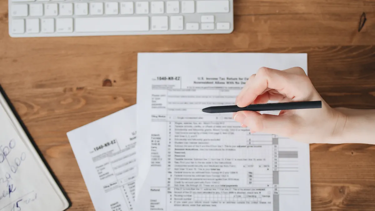 Estimated Taxes for Self-Employed Filers: Who Pays Hand with pen over tax forms on a desk